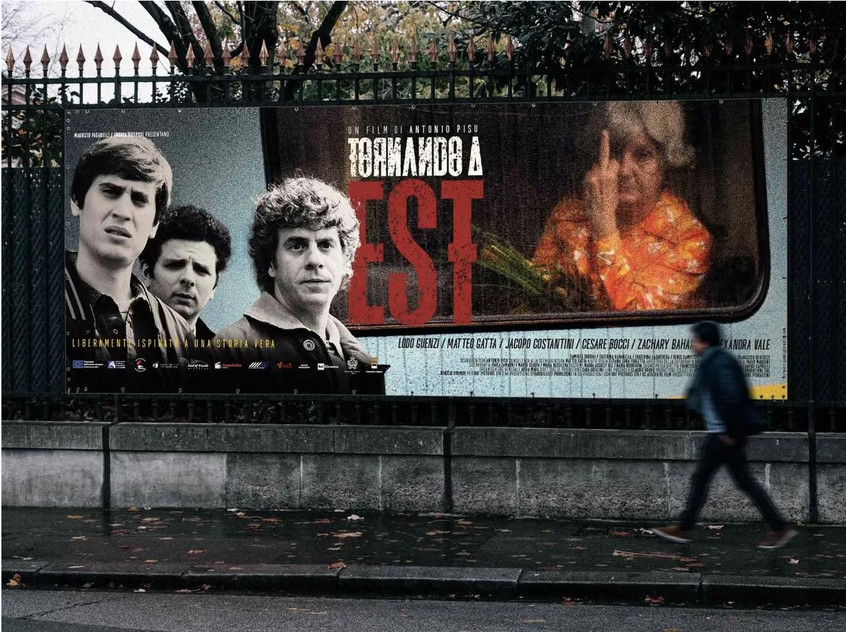 An Italian city street with a large Tornando a Est film billboard