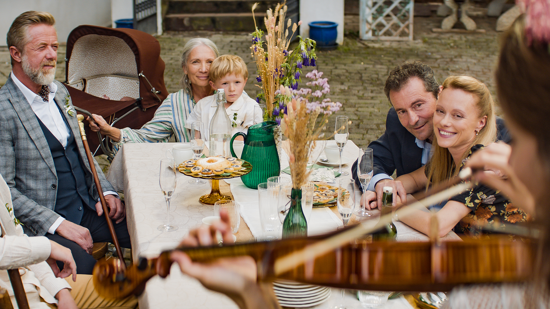 Friends and family gathered around a table with a violinist playing nearby